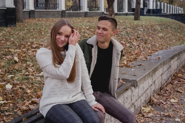 Pareja enamorada de pie sobre las hojas caídas de otoño en un parque, disfrutando de un hermoso día de otoño. Hombre abraza chica — Foto de Stock