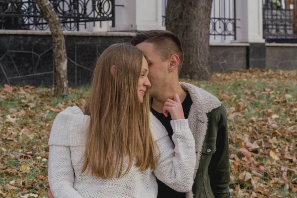 Couple in love stand on autumn fallen leaves in a park, enjoying a beautiful autumn day. Man hugs girl — Stock Photo, Image