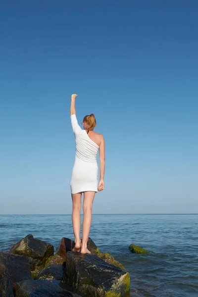Ελευθερία νεαρή γυναίκα απλωμένα χέρια σε παραθαλάσσιο βράχο άκρο γκρεμό. Γυναίκα με λευκό φόρεμα — Φωτογραφία Αρχείου