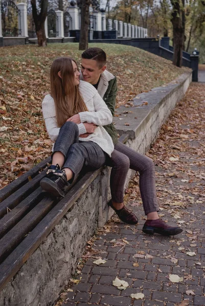 Couple in love stand on autumn fallen leaves in a park, enjoying a beautiful autumn day. Man hugs girl — Stock Photo, Image