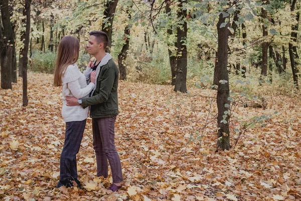 Verliebte Paare stehen auf herbstlichem Laub in einem Park und genießen einen schönen Herbsttag. Mann umarmt Mädchen — Stockfoto