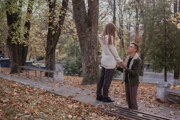 Pareja enamorada de pie sobre las hojas caídas de otoño en un parque, disfrutando de un hermoso día de otoño. Hombre abraza chica — Foto de Stock