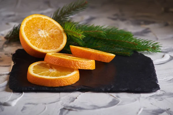 Frische geschnittene Orangen und Fichtenzweige auf grauem Hintergrund — Stockfoto