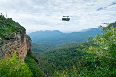 BLUE MOUNTAINS, AUSTRALIA - JANUARY 11, 2018: Tourists in the skyway going on the Three Sisters. Popular tourist attraction in Blue Mountains which offer a unique panoramic view through a glass floor while you glide between cliff tops in Jamison Vall clipart