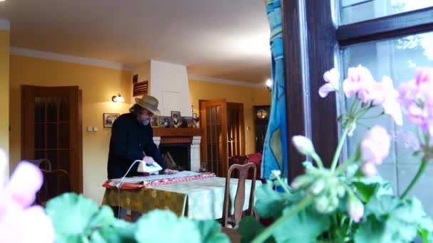 Homme célibataire pressant des vêtements dans le salon. Vue par la fenêtre . — Video