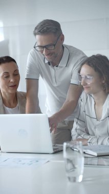 Business people team collaborating and analyzing data on a laptop during an office meeting, uniting efforts to reach shared objectives and drive successful outcomes together.