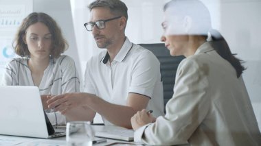 Professional team working together, reviewing digital analytics on laptop screen while strategizing corporate project details in modern workplace environment