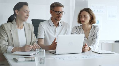 Business people team collaborating on a project, analyzing data on a laptop during a productive office meeting, demonstrating teamwork and problem solving skills.