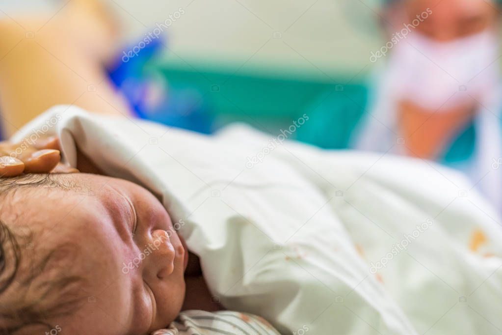 Cute newborn baby boy just after childbirth and doctor in the background