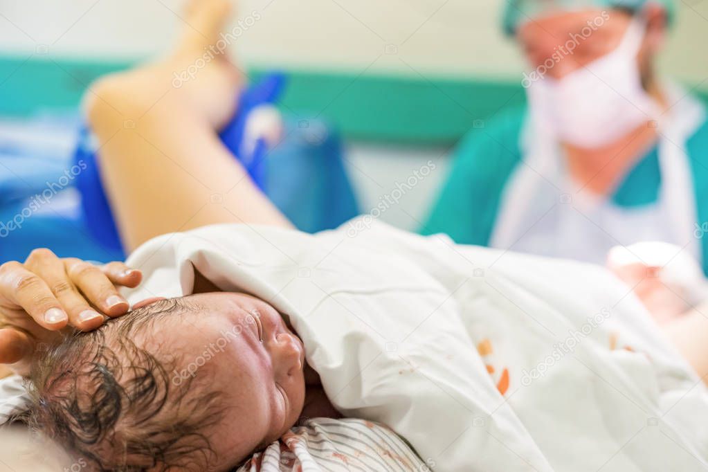 Cute newborn baby boy just after childbirth and doctor in the background