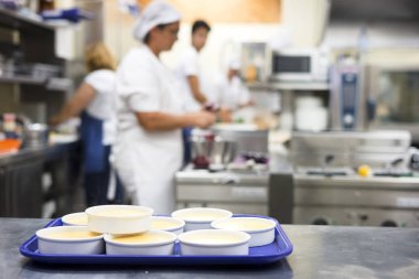 Creme Brulee ve arka plan olarak mutfakta çalışan personel ile çok sayıda yuvarlak kase 