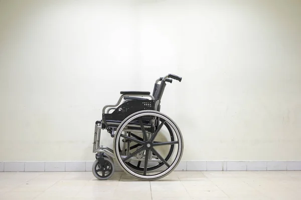 Empty wheel chair on sad, dark white background of hospital wall