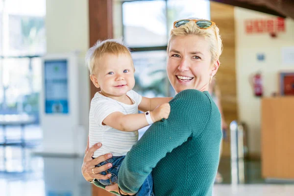 Madre sonriente sosteniendo al niño en el vestíbulo del hotel — Foto de Stock