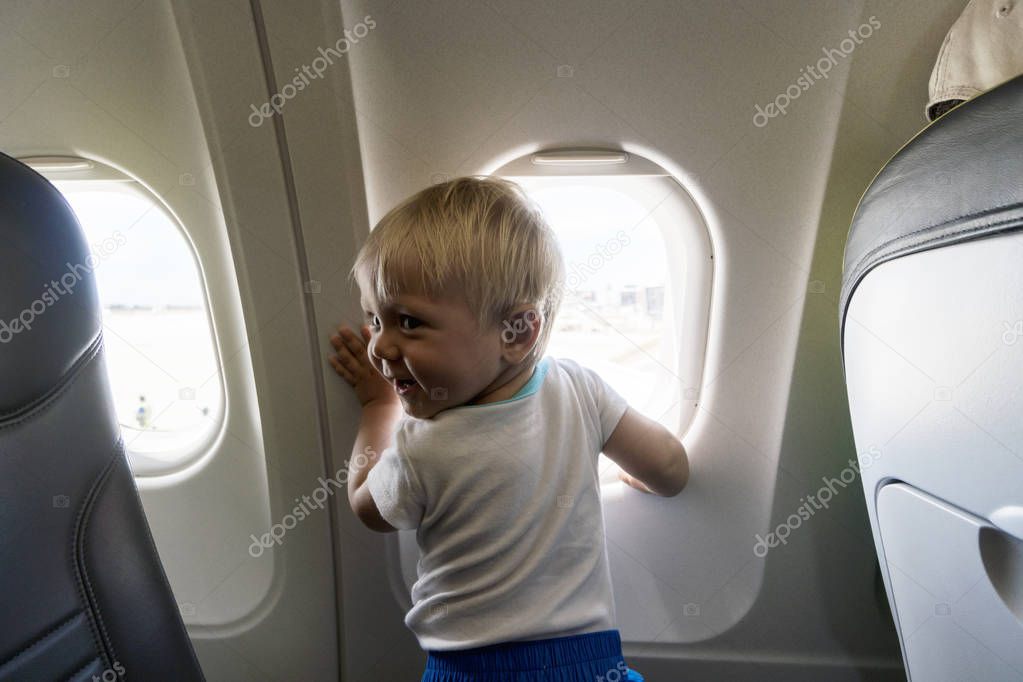 Happy one year old baby boy next to airplain's window 