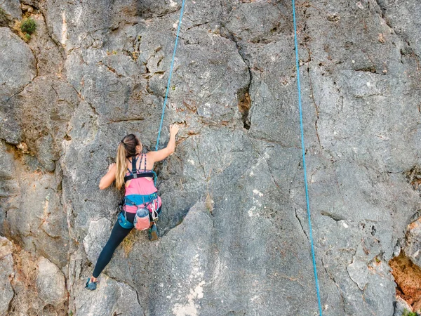 A woman in harness climbing a steep rock in Portugal