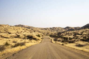 A road Spreetshoogte Pass in Namibia, with a gravel road winding through golden grassland and rocky hills under a bright, clear sky.