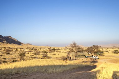 The vast Namib Desert from Spreetshoogte Pass, with hazy plains, rugged mountains, and a lone house on the ridge under the bright sky.