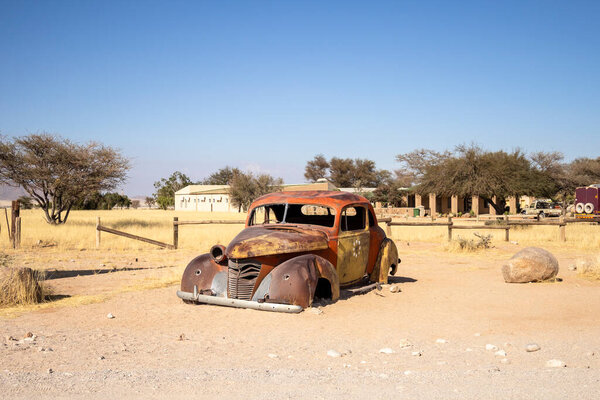 Solitaires car graveyard in Namibia features rusted vintage cars near small desert buildings,  set against dunes and mountains, capturing desert charm and isolation.