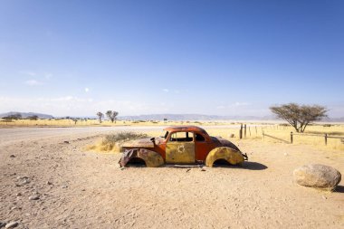 Solitaires car graveyard in Namibia features rusted vintage cars near small desert buildings,  set against dunes and mountains, capturing desert charm and isolation.