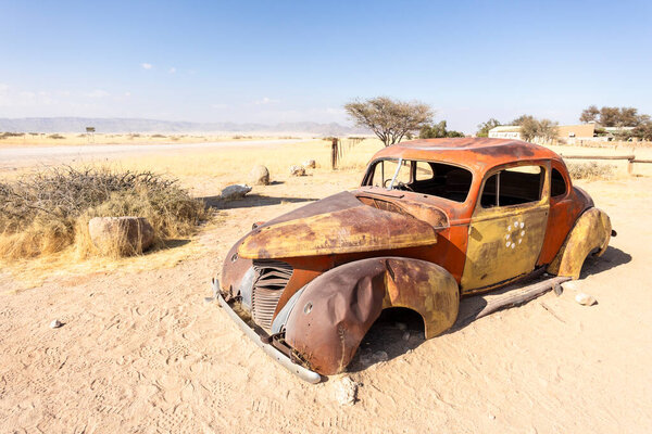 Solitaires car graveyard in Namibia features rusted vintage cars near small desert buildings,  set against dunes and mountains, capturing desert charm and isolation.