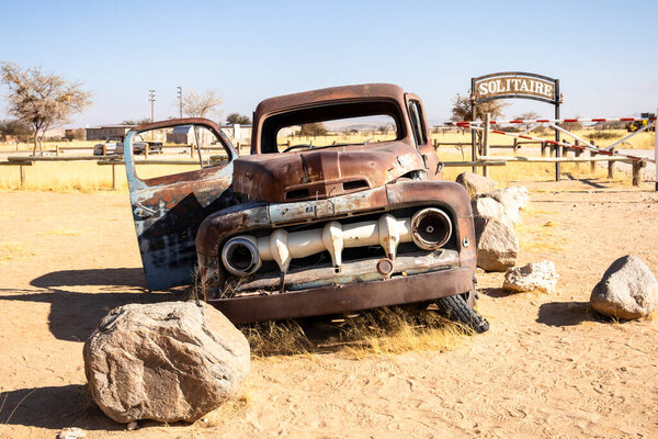 Solitaires car graveyard in Namibia features rusted vintage cars near small desert buildings,  set against dunes and mountains, capturing desert charm and isolation.