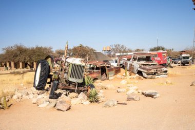 Namibya 'daki Solitaire araba mezarlığı - 27 Ağustos 2025: küçük çöl binaları yakınlarındaki paslı klasik arabalar, kum tepeleri ve dağlara karşı dizilmiş, çöl cazibesini ve izolasyonu yakalayan.