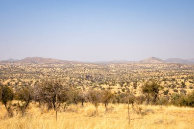 A sweeping view of Windhoek, Namibia, where  a desert landscape under a clear blue sky, framed by dry hills, scattered vegetation, and distant mountains.