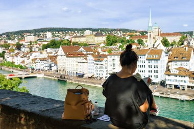 Zürih, İsviçre - 2 Eylül 2016: Zurich, İsviçre için bir rehber kitap bakarak ve Lindenhof Hill'de oturan kız. Limmatquai'de ve arka planda Predigerkirche