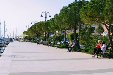Izola, Slovenya - 24 Nisan 2018: Slovenya'nın Adriyatik Denizi'ndeki Izola Marina'da setin üzerinde banklarda oturanlar