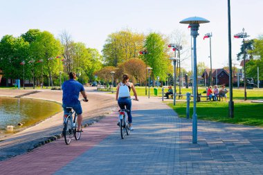 Nida, Lithuania - May 10, 2016: Couple riding a bicycle. Nida resort town near Klaipeda in Neringa, in the Curonian Spit and the Baltic Sea in Lithuania. clipart