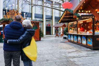 Senior Couple at Christmas Market at Kaiser Wilhelm Memorial Church in Winter Berlin, Germany. Advent Fair Decoration and Stalls with Crafts Items on the Bazaar. clipart