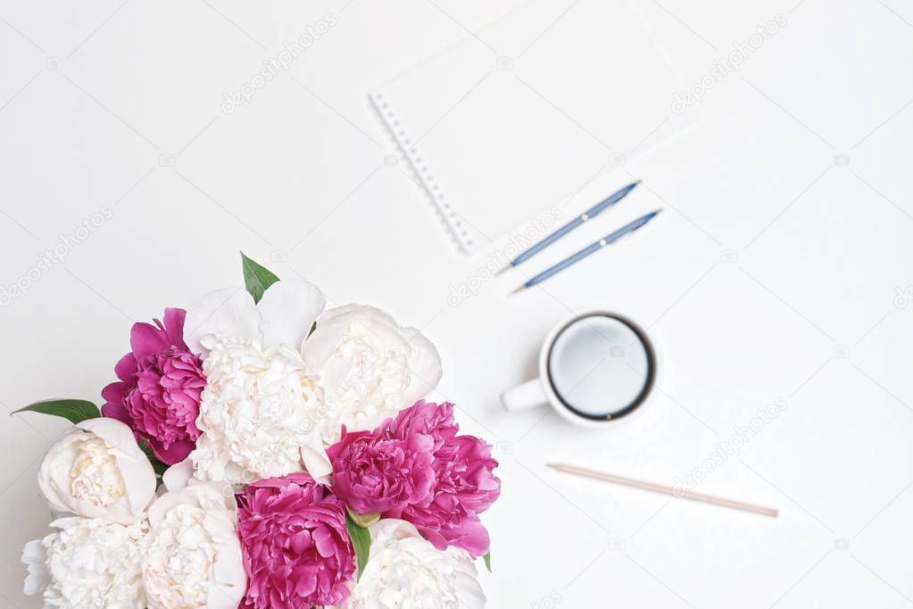 Workplace with coffee cup, paper, pen and pink and white peony flowers on white table background. Flat lay, top view