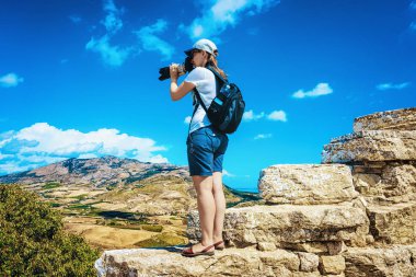 Sırt çantalı bir kadın İtalya 'nın Sicilya adasındaki Yunan tiyatrosunda Segesta manzarasına bakıyor.