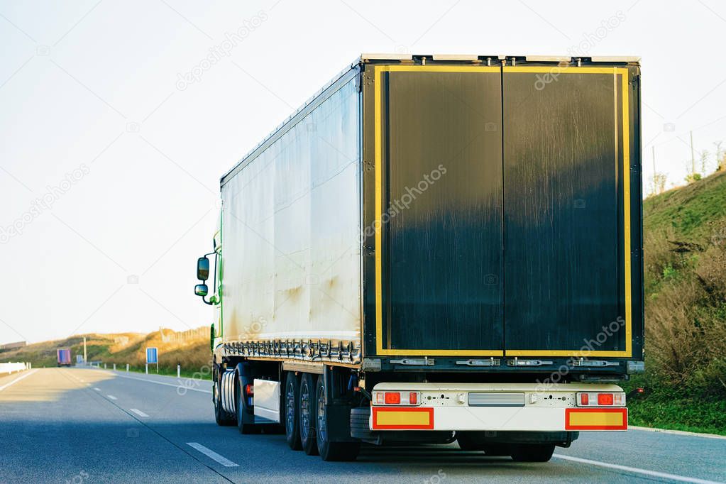 Black Truck in the asphalt road of Poland. Lorry transport delivering some freight cargo.