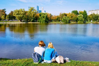 Novodevichy Pond 'daki parkta oturan genç kızlar Moskova' daki gökdelenlere bakıyorlar.