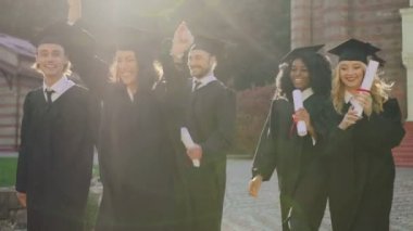 Güneşli bir diploma ile onların Üniversite binası dışarı mutlu bir şekilde yürürken neşeli gülümsüyor ve erkek karışık ırklar mezunları. Açık havada