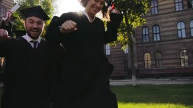 Karışık ırklar arkadaşları mezuniyet siyah ve mutlu bir şekilde çalıştıran kapaklar ve sevinçle güneşli bir günde onların Üniversitesi'nden. Dışarıda