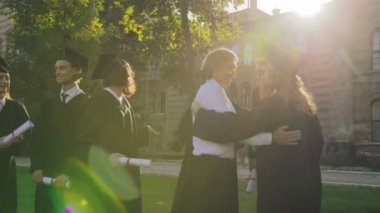 Gri saçlı orta yaşlı adam tebrik ediyor ve erkek mezunları karışık ırklar ile onların Üniversitesi'nden mezun güneşli bir günde. Açık