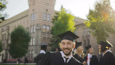 Poz ve University yakınındaki mezuniyet gününde elinde diploma ile kamera önünde atlama mutlu ve neşeli bir genç adam. Dışarıda