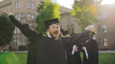 Neşeli erkek lisansüstü mezuniyet gününde onun tatlı kamera önünde gösterilen. Arkadaşları arka planda. Açık