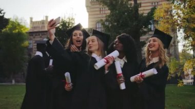 Karışık ırklar siyah geleneksel önlük ve arka bina güzel üniversite Smartphone'da selfies yapma kapaklar kızlar mezun oldu. Dışarıda