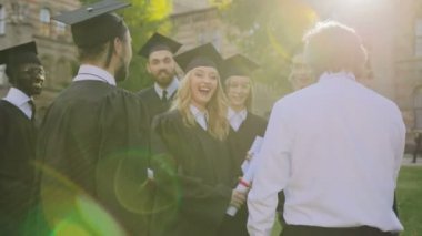 Orta yaşlı adam siyah önlük ve kapaklar ve mezunları grubuna geliyor ve onları törenden sonra diploma almak ile tebrik ediyor. Açık havada