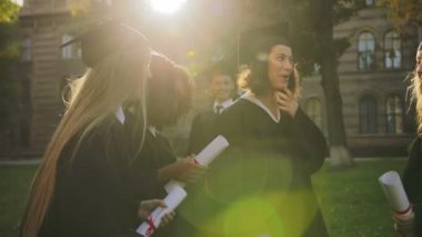 Güzel çok etnik önlük kızlarda mezun oldu ve onların diplomalar holding ve sevinçle konuşurken kapaklar University yakınındaki. Çocuklar arka planda. Açık havada