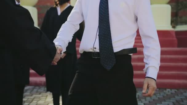 Homem bonito de cabelos grisalhos parabenizando o jovem em roupas especiais com a obtenção de um diploma na graduação. Fora — Vídeo de Stock