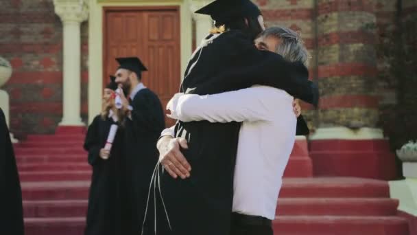 Gray-haired goed uitziende vader feliciteren met haar dochter in speciale kleding met het afstuderen bij de ingang van de Universiteit. Buiten — Stockvideo