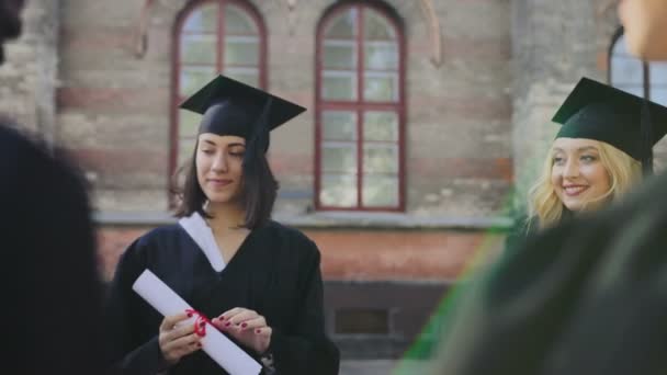 Manliga och kvinnliga utexaminerade chattar utanför universitetet på graduation dagen. Multi etnisk grupp människor — Stockvideo
