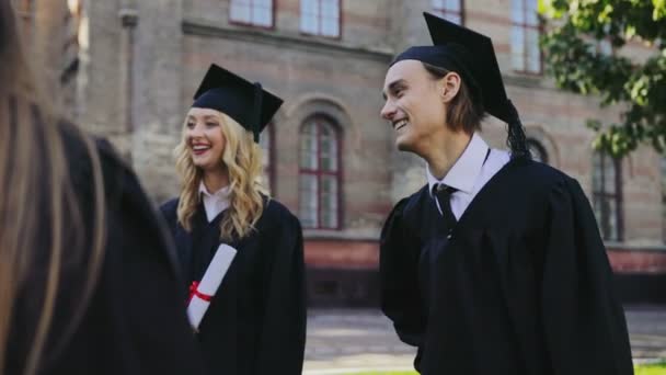 Radostné absolventů v tradiční šaty a čepice diskutovat o něco po promoci před univerzitou. Vně — Stock video