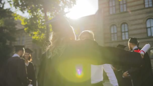 Dahinter die blonde Absolventin, die an einem sonnigen Tag von ihrem grauhaarigen Vater zum Abschluss beglückwünscht wird. Außen — Stockvideo