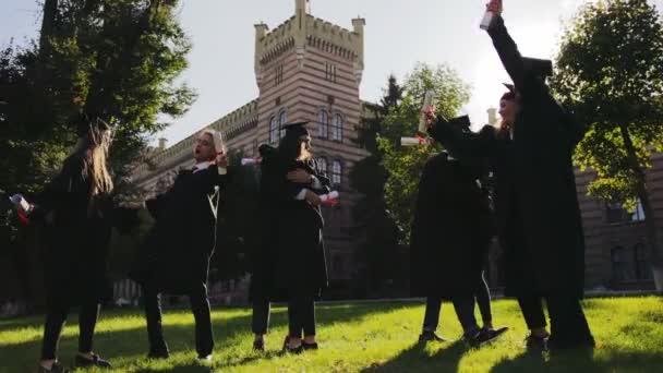Kevert emberfajták boldog diplomások átölelve, és gratuláltak egymásnak vidáman az érettségi nap az Egyetem előtt. A szabadban — Stock videók