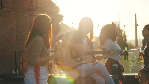 Handsome young man playing on the guitar and singing among his friends on the rooftop party. The brick wall background. Outside. Mixed races — Stock Video